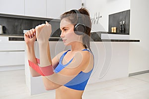 Portrait of determined beautiful woman, listening music, workout with elastic resistance band, doing exercises on arms