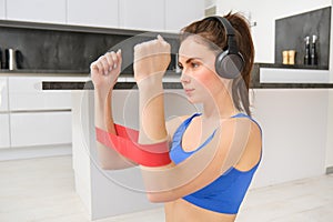 Portrait of determined beautiful woman, listening music, workout with elastic resistance band, doing exercises on arms