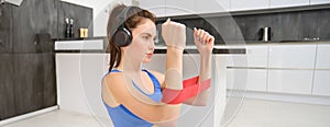 Portrait of determined beautiful woman, listening music, workout with elastic resistance band, doing exercises on arms