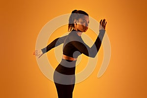 Portrait of determined black woman exercising, running over orange neon background, studio shot, free space