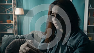 Portrait of a devastated, lonely woman who is sitting on the sofa in the living room close up. A woman desperately