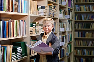 portrait of diligent caucasian child boy with book between bookshelves in campus library