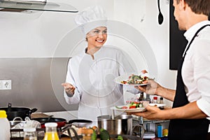 Woman cook giving to waitress ready to serve salad