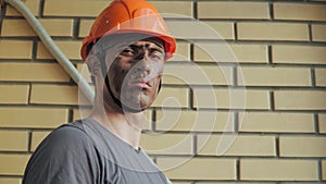 Portrait Dirty Building Worker on Background of a Brick Wall. Handsome Serious Man in a Hard Hat. Filthy Job and Physical labor