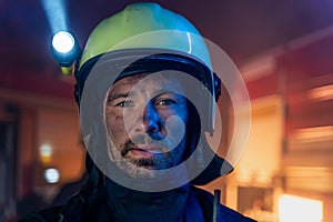 Portrait of dirty firefighter man on duty with fire truck in background at night, looking at camera.