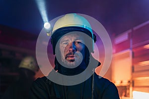 Portrait of dirty firefighter man on duty with fire truck in background at night, looking at camera.