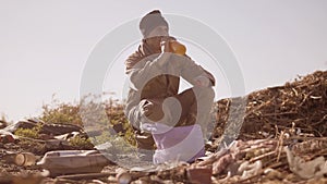 Portrait of a dirty homeless hungry man in a dump drinks the missing juice in the package with walking goes looking for