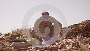 Portrait of a dirty homeless hungry man in a dump eating for food in the package with walking goes looking for food slow