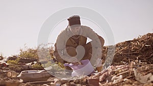 Portrait of a dirty homeless hungry man in a dump eating for food in the package with walking goes looking for food slow