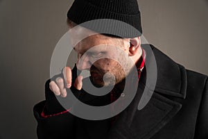 A portrait of a dirty man who put his finger in his nose. The concept of a homeless sleazy beggar in black clothing