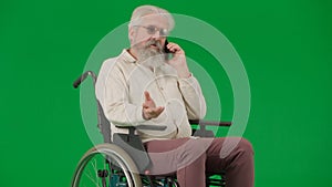 Portrait of disabled man isolated on chroma key green screen background. Senior man sitting in wheelchair talking on