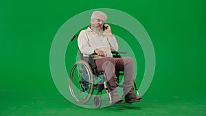 Portrait of disabled man isolated on chroma key green screen background. Senior man sitting in wheelchair talking on