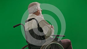 Portrait of disabled man isolated on chroma key green screen close up. Senior man sitting in wheelchair with his back at