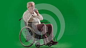 Portrait of disabled man isolated on chroma key green screen full shot. Senior bearded man sitting in wheelchair holding