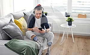 Portrait of disabled young man using smartphone indoors at home, leg prosthetic concept.
