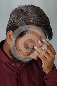 Portrait of a disappointed adult South Asian man with graying hair against a gray wall