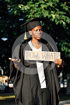 Portrait of disappointed afro american guy holding cardboard poster and lending hand on street. Looking for job, hiring