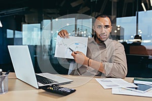 Portrait disappointed businessman inside office, african american man showing document graph with bad financial