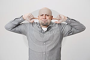 Portrait of disappointed sad man covering his ears with hands over white background. Male expresses his disgust of what