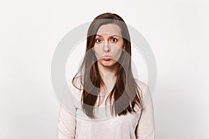 Portrait of disconcerted displeased offended young woman in light clothes blowing lips isolated on white wall background