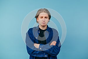 Portrait of a disgruntled guy in a blue shirt stands on a blue background and looks suspiciously at the camera, wearing a shirt