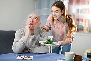 Portrait of a disgruntled man, to whom a young woman brought a plate of spinach