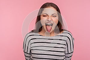 Portrait of disobedient funny woman in striped sweatshirt showing tongue out, expressing displeasure, teasing