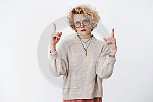Portrait of displeased and angry frustrated young european blond woman in glasses and sweater frowning gloomy pointing