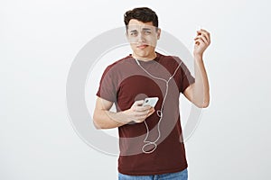 Portrait of displeased shocked attractive man in casual outfit, putting out earphones with disliking grimace, holding