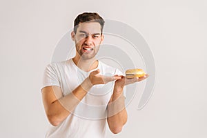 Portrait of displeased young man with disgust pointing to bad burger on white isolated background, looking at camera.