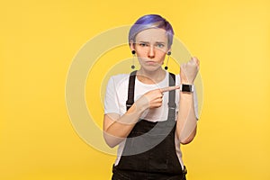 Portrait of dissatisfied angry hipster girl pointing watch on her wrist and looking impatient. yellow background, studio shot