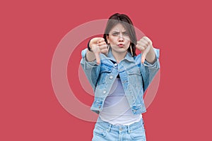 Portrait of dissatisfied beautiful brunette young woman with makeup in denim casual style standing, thumbs down and looking at