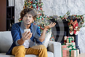 Portrait of dissatisfied upset man at home on Christmas and New Year holiday, hispanic looking disappointed at camera