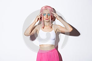 Portrait of distressed caucasian girl with pink wig and party makeup, standing with closed eyes and touching head