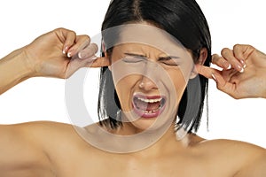 Portrait of disturbed young woman shouting while putting fingers on the ears