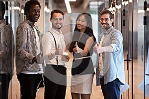 Portrait diverse employees standing in office hallway, showing thumbs up