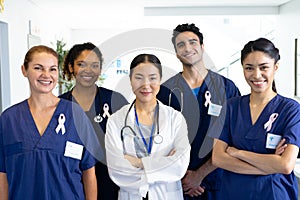 Portrait of diverse group of healthcare workers wearing cancer ribbons smiling in hospital corridor