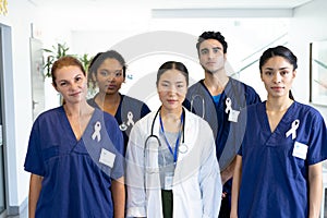 Portrait of diverse group of healthcare workers wearing cancer ribbons standing in hospital corridor