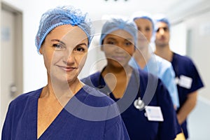 Portrait of diverse group of healthcare workers wearing surgical caps smiling in hospital corridor