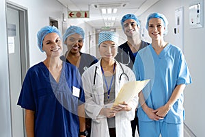 Portrait of diverse group of healthcare workers wearing surgical caps smiling in hospital corridor