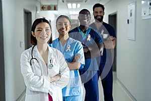 Portrait of diverse group of smiling healthcare workers wearing cancer ribbons standing in corridor