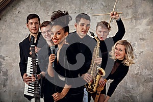 Portrait of diverse group of young people musical band playing with instruments - on gray concrete background.