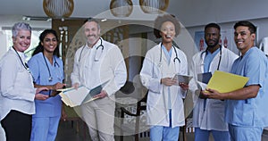 Portrait of diverse male and female doctors standing in hospital corridor smiling to camera