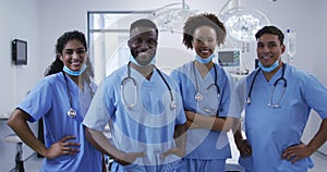 Portrait of diverse male and female doctors standing in operating theatre smiling to camera