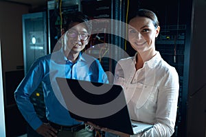 Portrait of diverse male and female engineers with laptop smiling in computer server room