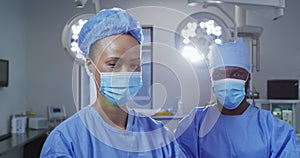 Portrait of diverse male and female surgeon wearing face masks standing in operating theatre