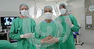 Portrait of diverse male surgeons wearing surgical gowns in operating theatre, slow motion