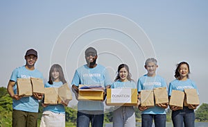 portrait diverse of people in volunteer blue t-shirt holding donation box and donated items standing in the park