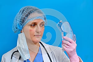 Portrait of a doctor with cuts and wounds from goggles. Close-up of a nurse in a medical mask on a blue background with traces of