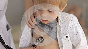 Portrait of a doctor examining heartbeat of the kid with stethoscope.